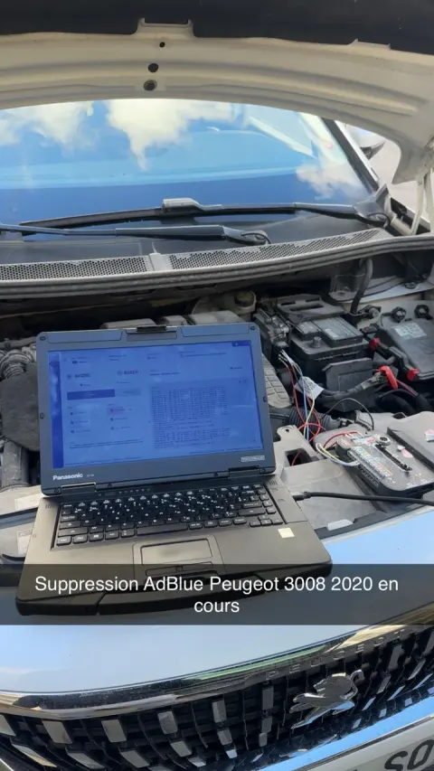 Ordinateur de diagnostic posé dans le compartiment moteur ouvert d'un Peugeot 3008